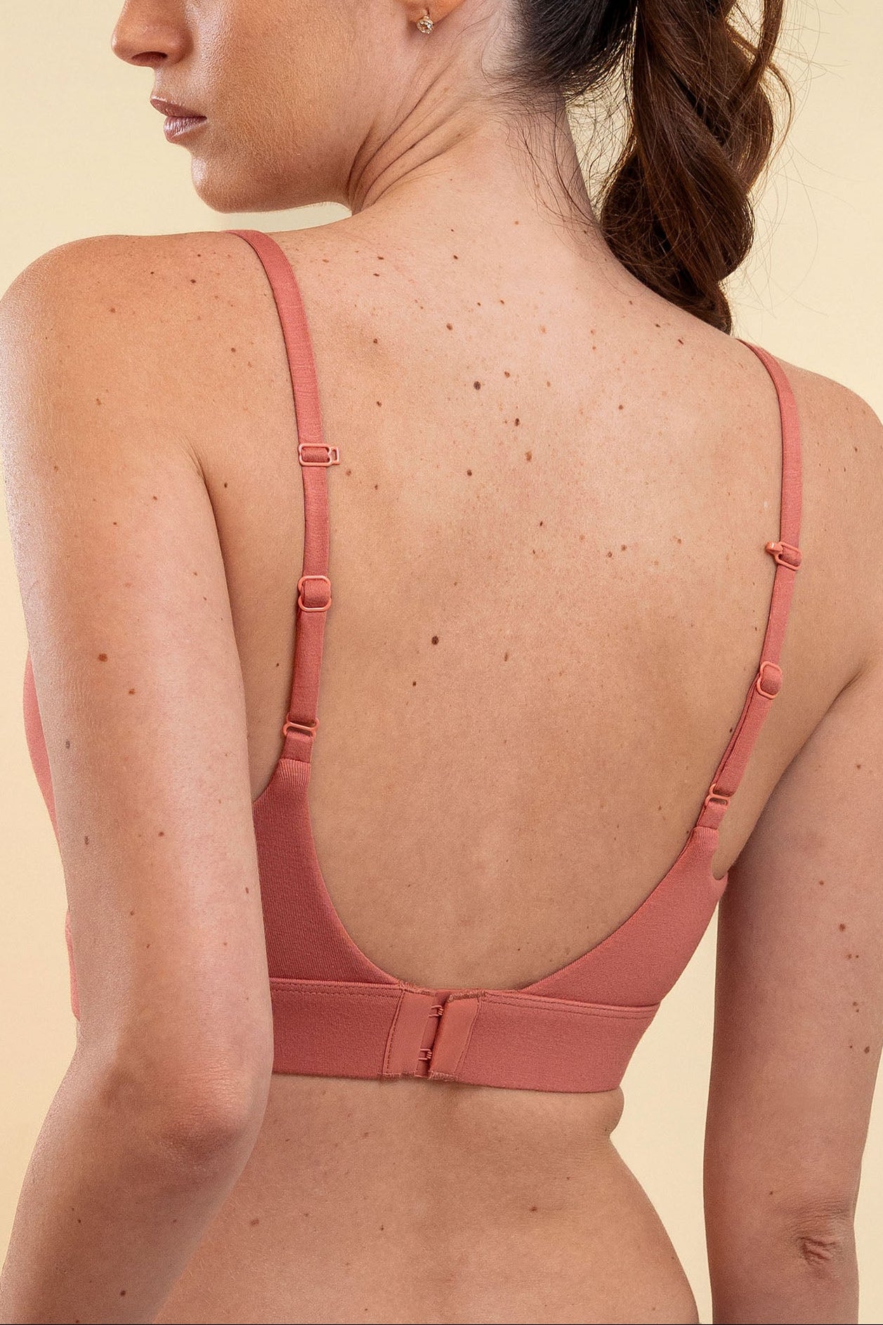 Woman wearing a pink bralette against a beige background