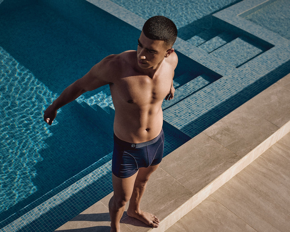 Man standing by a pool wearing dark blue boxer brief.