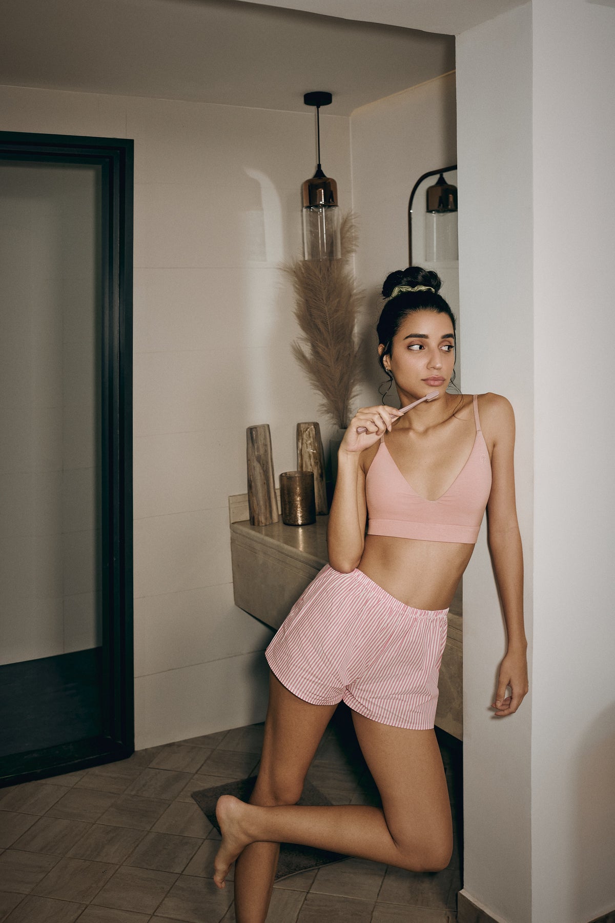 Woman in pink bra and shorts standing in a room with minimal decor.