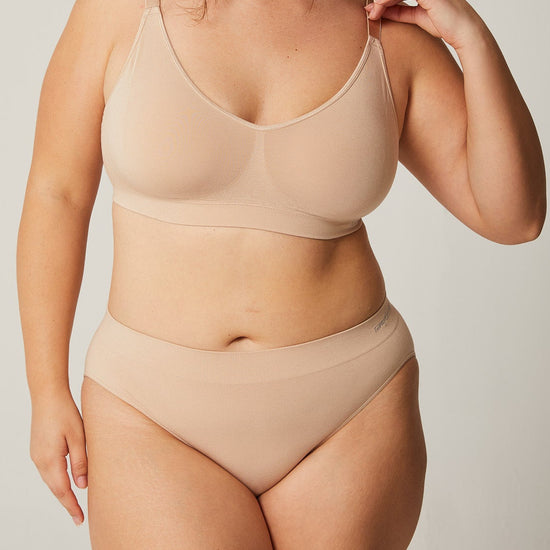 Woman wearing a beige bra and panties set against a plain background