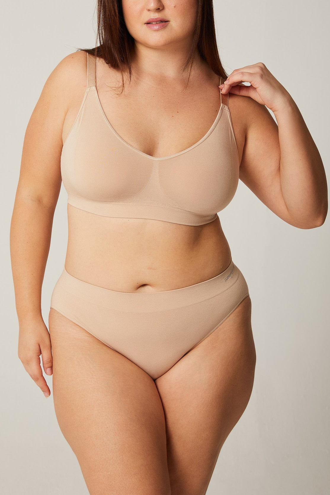 Woman wearing a beige bra and panties set against a plain background