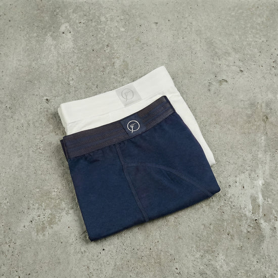 Two pairs of men's underwear, one navy and one white, on a concrete surface.