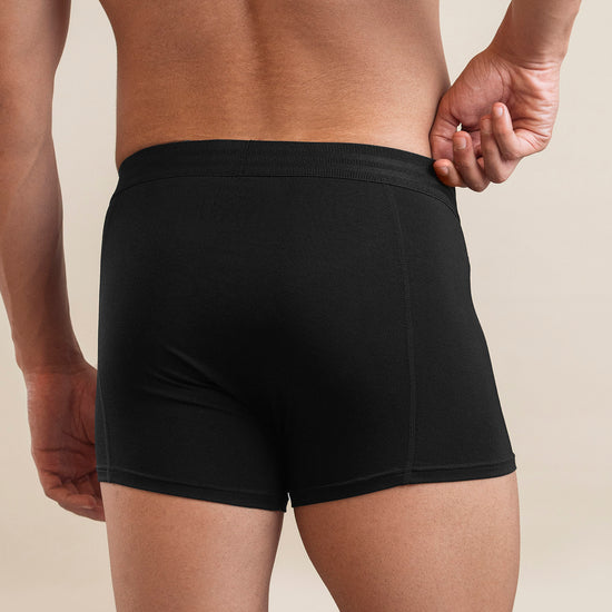 Black boxer briefs worn by a person on a beige background