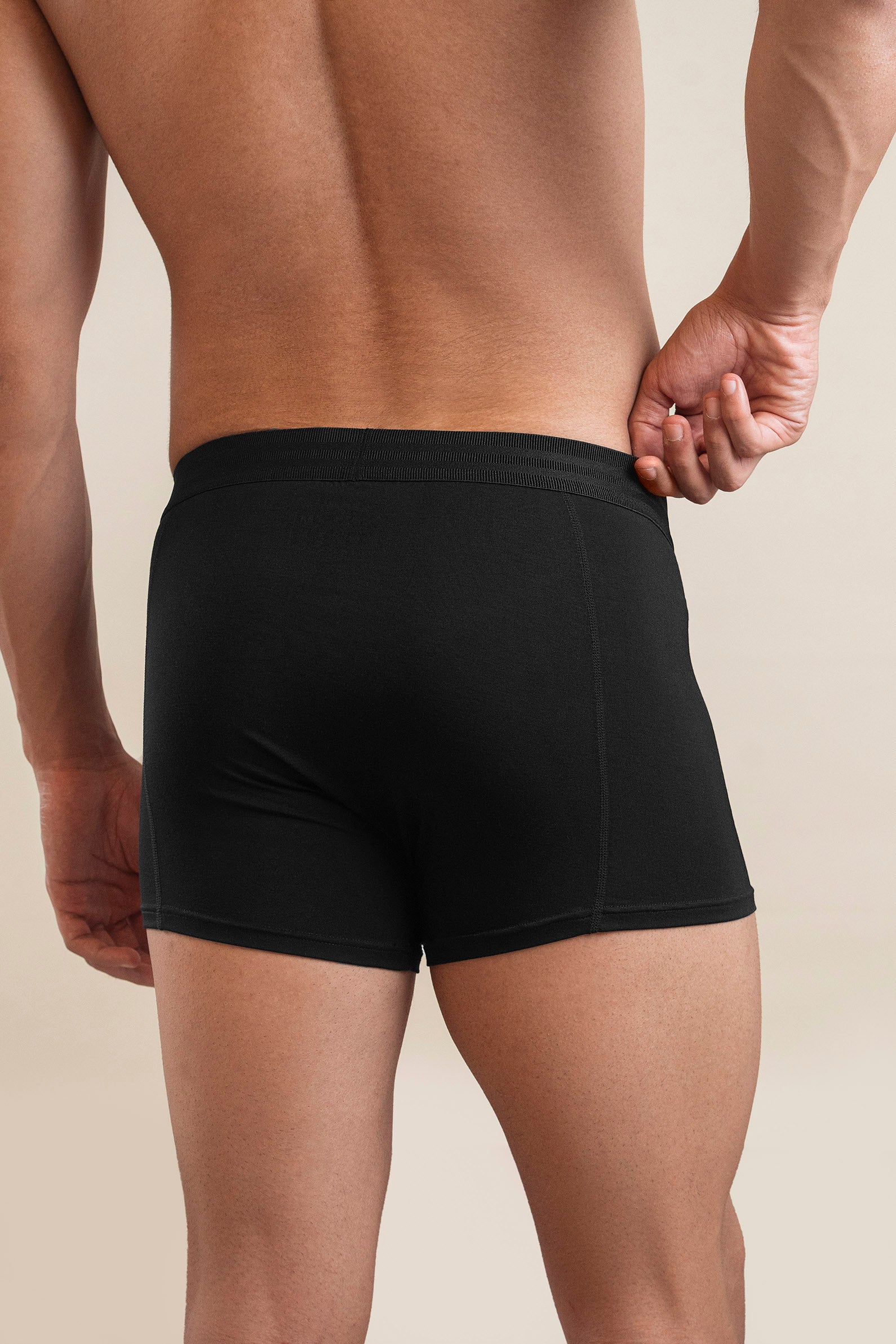 Black boxer briefs worn by a person on a beige background