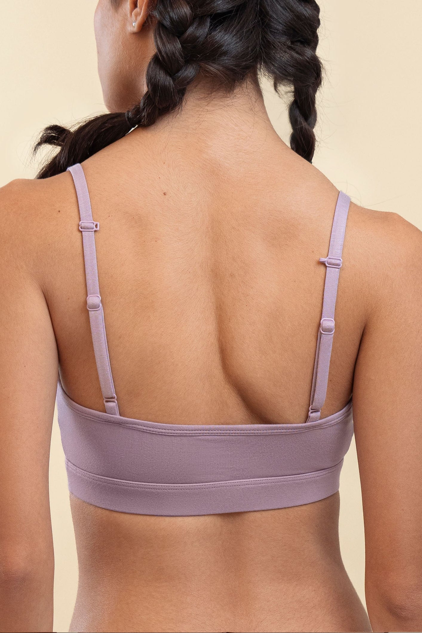 Person wearing a light purple bralette on a beige background