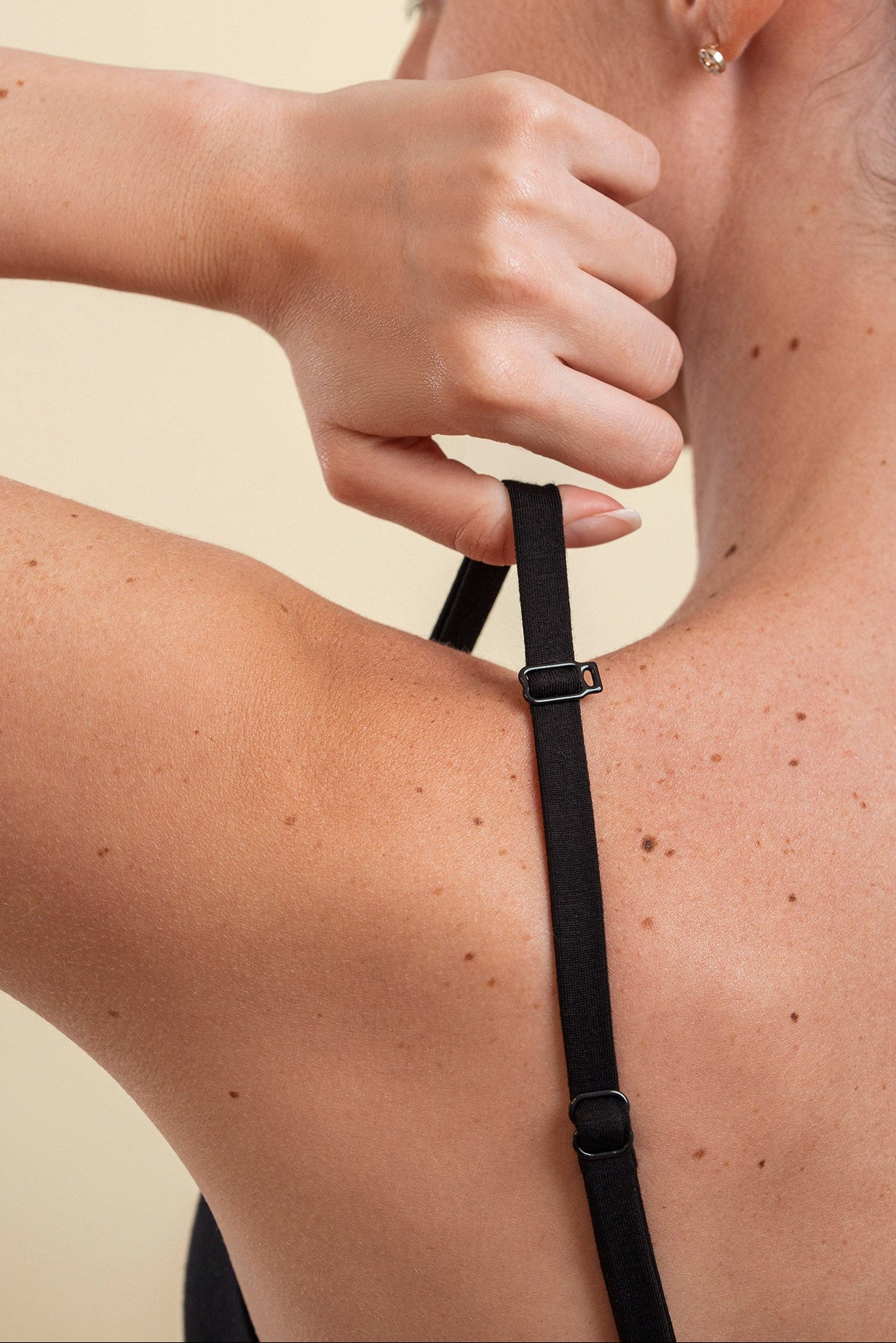 Woman adjusting a black strap on their shoulder against a beige background