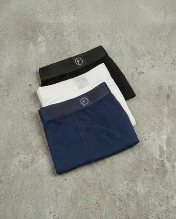 Three pairs of men underwear in black, white, and navy on a concrete surface.
